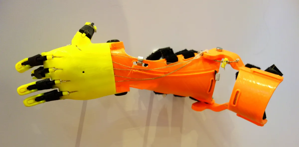 A yellow and orange e-NABLE Raptor Reloaded prosthetic hand, shown as an accessibility reference project